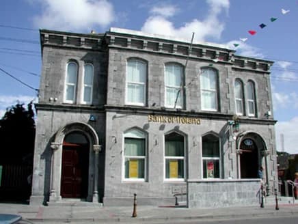 Ein zweigeschossiges Eckgebäude aus behauenem Kalkstein, Rundbogenfenster, die Worte Bank of Ireland in den Fries gemeißelt.